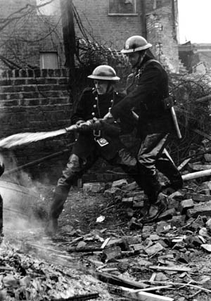 Richard Southern and R.H. Betts, auxiliary firemen in London, train their hoses on a flaming house while another burns just behind them. A number of firefighters died during the Blitz.