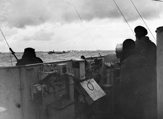 This photograph, taken from the deck of the British cruiser Bellona, depicts a number of merchant vessels laden with supplies en route to the Soviet Union. During this particular voyage, a German U-boat was sunk by escort vessels and several German aircraft were shot down while attacking the convoy.