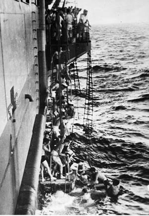British sailors aboard the escort carrier HMS Trouncer use a carley float to assist the survivors of the sunken merchant vessel SS Empire Patrol, many of whom are women. The Empire Patrol had caught fire during an effort to repatriate Greek refugees from Abyssinia. Of the 510 survivors of the sinking, HMS Trouncer rescued 420.