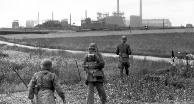 Near the town of Collombelles east of Caen, three German soldiers move across an open field toward a complex of factories and warehouses looming in the distance. These soldiers belong to Jager Regiment 32, which was incorporated into the 21st Panzer Division in July 1944.