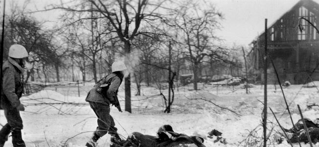 U.S. troops advance cautiously past the bodies of several dead German soldiers during combat on the outskirts of Jebsheim.