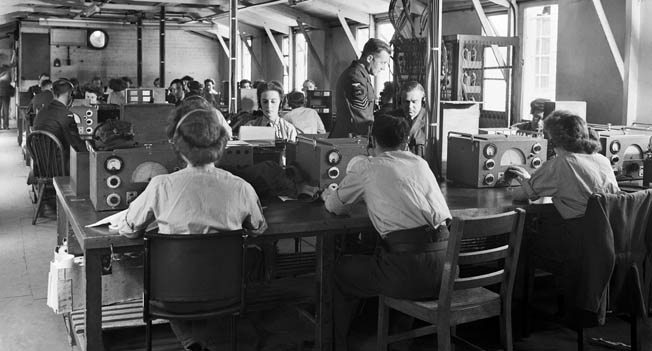 WAAF and RAF radio operators record meteorological reports from aircraft and ships in the wireless cabin of the central forecasting station at Dunstable, Bedfordshire. The Dunstable team, along with the teams at Bushey Park and Southwick, provided Stagg with constant weather updates. 