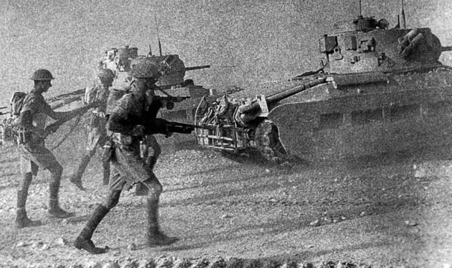 In this photograph, probably staged during a desert training exercise, soldiers of the Scots Guards advance behind British tanks.