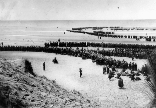 Awaiting rescue by sea, Allied soldiers form long lines on the beach at Dunkirk. The great effort mounted by military and civilian seamen resulted in nothing short of a miracle.