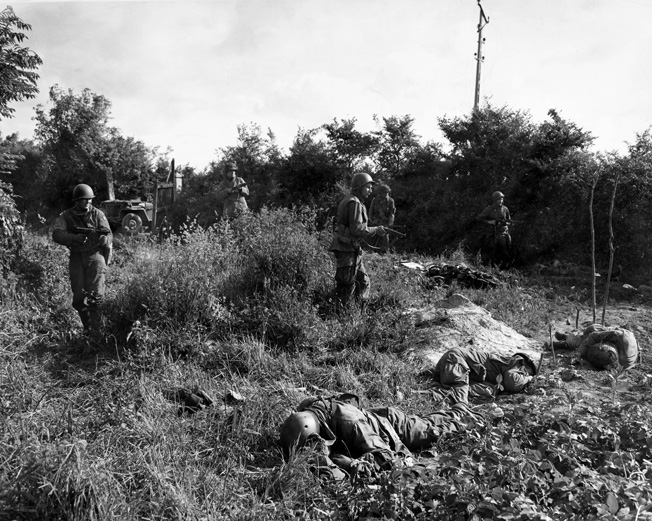 WORLD WAR II: FRANCE, 1944. American paratroopers move through a field in Carentan, France, passing members of their own unit killed by German snipers. Photographed 14 June 1944.