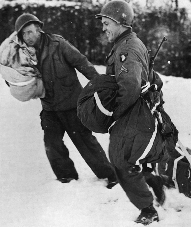 Defending Bastogne during bitter winter fighting, troopers of the 101st Airborne Division recover a canister of medical supplies which has been airdropped to the surrounded soldiers. the 101st held the crossroads town during the Battle of the Bulge until relieved by the 4th Armored Division.