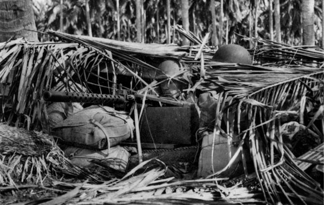 Camouflaged with palm fronds and reinforced with sandbags and coconut logs, a machine gun position on Guadalcanal is manned by alert Marines. During several massed attacks, waves of Japanese soldiers were mowed down by American machine guns. 