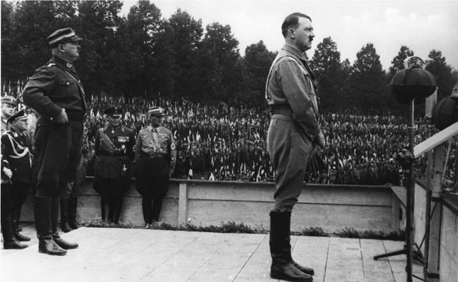 Hitler addresses an adoring throng during the Reich Party Rally of Victory held in Nuremberg from August 30 to September 3, 1933. Standing behind Hitler is his staunch supporter, Ernst Röhm, leader of the SA Stormtroopers who was murdered the following summer during the Night of the Long Knives.