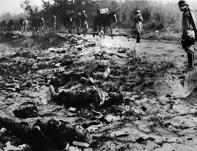 On the march toward the siege lines around the town of Myitkyina, Chinese soldiers pass the bodies of dead Japanese troops killed in earlier action against Allied troops.