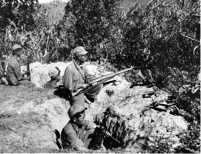 Kachin scouts defend their dug-in positions in Burma with an assortment of Allied weapons. The scout standing at center carries the British Short Magazine Lee-Enfield (SMLE) rifle. The scout at lower right holds an American M3 submachine gun, commonly known as the grease gun.