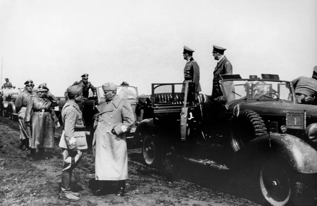 Benito Mussolini (foreground, center) speaking with commander Giovanni Messe, with Adolf Hiter (right) and field marshal Gerd von Rundtstedt in the truck beside them, during the inspection of Italian units near Uman (south of Kiev), Ukraine. At left is Nazi official Martin Bormann. Photograph, 28 August 1941.