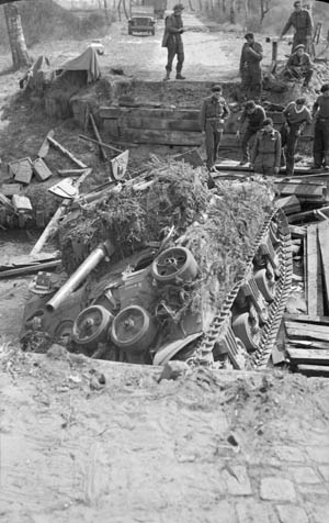 During the 21st Army Group drive toward the German city of Bremen, this Sherman tank attempted to cross a stream on an unstable bridge and collapsed it in the process. Armored vehicles that followed were compelled to seek another crossing point.