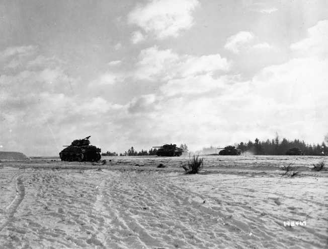 On January 1, 1945, American Sherman tanks fire their 75mm cannon at German positions in the Belgian countryside.