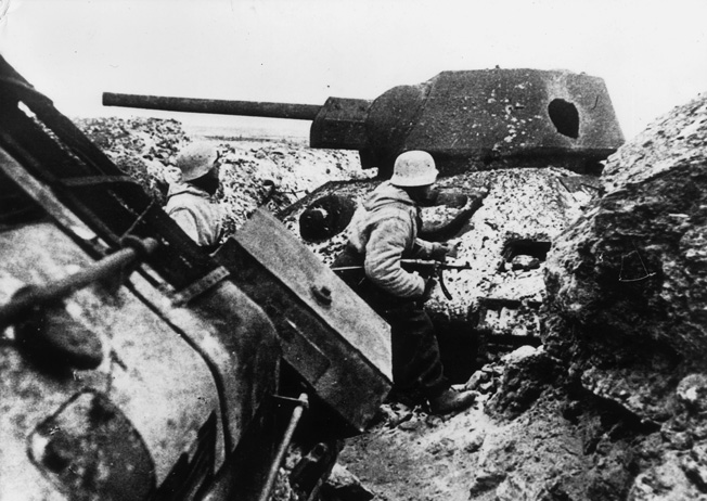 German soldiers pass one of scores of destroyed Red Army tanks near Leningrad. Although Russian losses in armor were severe, Soviet production capacity made good on their replacements.