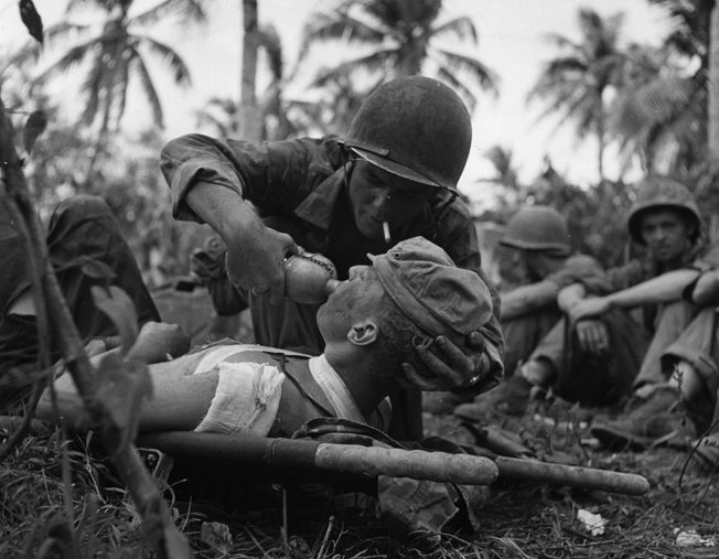 A Navy corpsman gives a drink of water to a wounded Marine on the island of Guam in the Pacific. In addition to the thousands of casualties treated by the U.S. Army medical personnel, the U.S. Navy also trained many for the war effort.