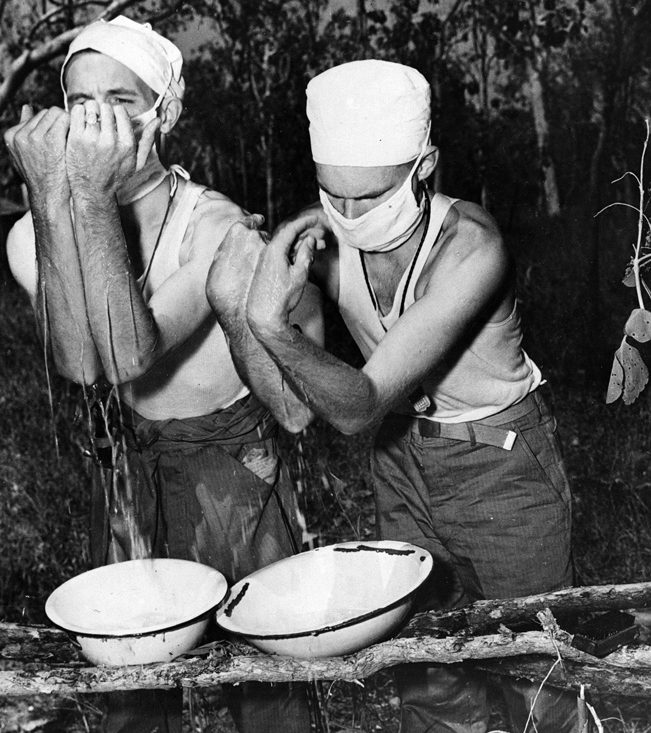 Two Army surgeons scrub up in preparation for a surgical procedure at a first aid station. Although significant advances were made in the treatment of casualties during World War II, conditions were often spartan.