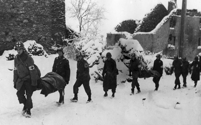 Medical Personnel of the U.S. 35th Infantry Division carry litters of wounded soldiers toward the rear near the snow-covered town of Lutrebois, Belgium.