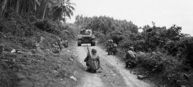 A Sherman tank accompanies soldiers of the 103rd Infantry Regiment, 43rd Division as they advance along a dirt road in the Philippines. Their mission was to clear the vicinity of Japanese troops who had ambushed an American column earlier in the day.