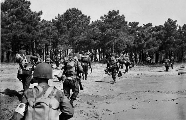 Hustling off the beach on the morning of August 15, 1944, American soldiers have just set foot in France during Operation Anvil-Dragoon. The cover of a nearby pine grove will serve as an area for orientation and rallying troops to their various commands.