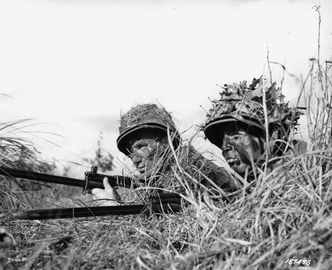 During training at the U.S. Army Ranger School in 1943, two soldiers are wearing the newly issued M1 helmet and liner. They have applied grass and leaves as camouflage.