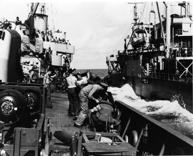 Coastguardsmen aboard the Taney manhandle a fuel hose during a refuel from a U.S. Navy oiler.