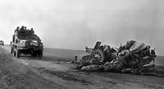 Wheeled vehicles of the U.S. 4th Armored Division speed past a destroyed German artillery piece and the dead crew sprawling beside it. German troops and equipment that dared to move in daylight were often the targets of Allied fighter-bombers, which wreaked havoc and caused heavy casualties during the final months of the war in Europe.