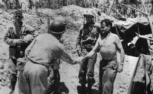 General Geiger, back to camera, shakes hands with Colonel Lewis Puller at the 1st Marine Regiment command post. Brigadier General Oliver Smith is behind Puller. 