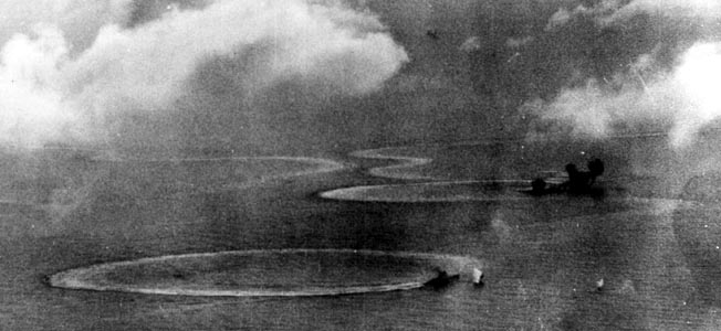 Taking evasive action against American dive-bombers and torpedo planes, a Japanese heavy cruiser turns in a clockwise circle. In the distance the plumes of two bomb hits on a Kongo-class battleship are visible, while the stricken vessel narrowly averts a collision with an aircraft carrier also caught in the relentless air attack. Note the thick antiaircraft fire from the Japanese warships and the telltale patterns of their frantic maneuvers in the water.