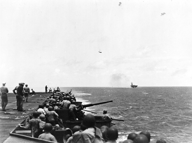 A Japanese plane, hit by anti-aircraft fire from USS Bunker Hill and USS Cabot, falls toward the water in flames.