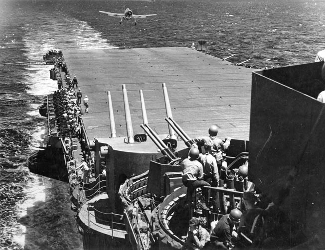 Low on fuel, a Grumman F6F Hellcat fighter lands on the deck of the USS Lexington during the Battle of the Philippine Sea. Antiaircraft gunners are seen at battle stations aboard the carrier.