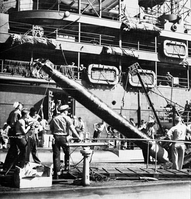 Using a crane to lower a torpedo through their submarine's forward torpedo hatch, U.S. submariners position the weapon to be moved onto a skid with rollers and then along a track to storage racks or directly into the torpedo tube.