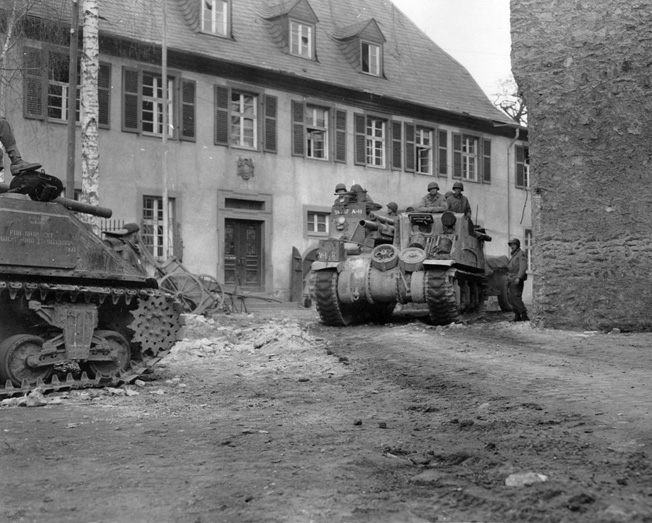 Tanks of the 9th Armored Division roll through an abandoned French village.