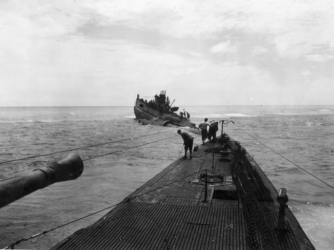 Several attempts to free the Dutch submarine O-19 from the reef on which it had run aground proved unsuccessful. In this photo, American sailors watch the progress in attaching the towline to the marooned vessel.