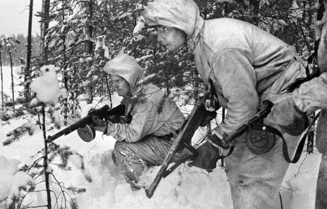 Finnish soldiers wearing camouflage suits watch for movement along a forest road as the Soviet Red Army advances into their country.