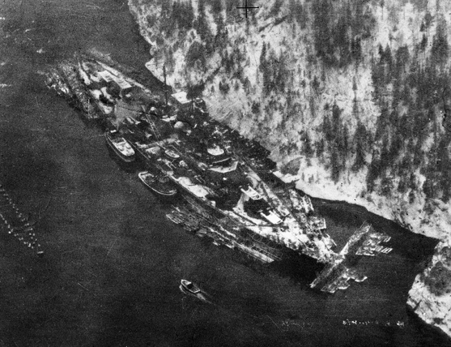 Obscured by camouflage netting, the German super battleship Tirpitz was nevertheless caught in the lens of a RAF reconnaissance aircraft while anchored in Aas Fjord in February 1942. The immense size of the battleship is apparent in this photograph.
