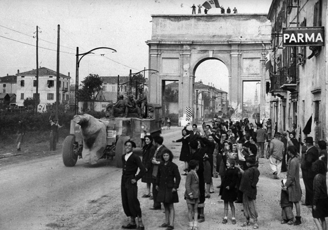 The citizens of Parma in northern Italy line the streets to cheer the advancing Allied columns pursuing the retreating Germans. Here, a towed 155mm howitzer makes its way down the street amid the gathering of well wishers.