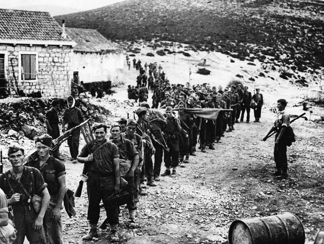 Trained by British instructors on an island in the Adriatic Sea, Yugoslav partisans sing martial music as they march toward a German schooner that will transport them to participate in a raid on a German communication center.