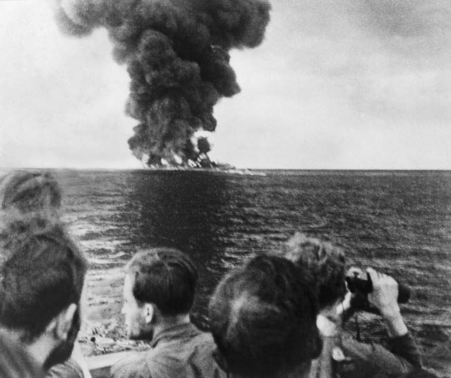 Crewmen of a German U-boat watch a blazing tanker burn to the waterline after their torpedo attack. During Operation Drumbeat, U-boats ranged along the U.S. East Coast, attacking merchant shipping with impunity.