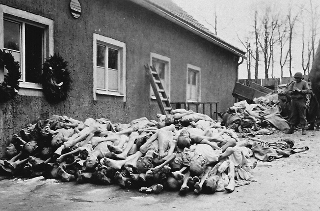 An American soldier surveys a pile of corpses outside the Buchenwald crematorium.