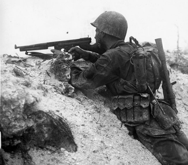 A Marine fires his Thompson submachine gun at Japanese positions from the shelter of a sandbank on Peleliu. 