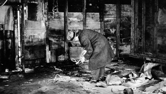 An inspector looks at evidence of a Black Market meat operation in a filthy building. The black marketeers spread lime on the floor in a poor attempt at cleanliness. 