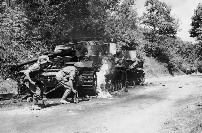 Men of the 2/6th Queen’s Regiment advance past a burning German PzKpfw IV tank in the Salerno area, September 22, 1943.