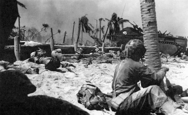 U.S. Marines, taking cover behind the low sea wall on Tarawa, watch as an amtrac advances toward an enemy position.