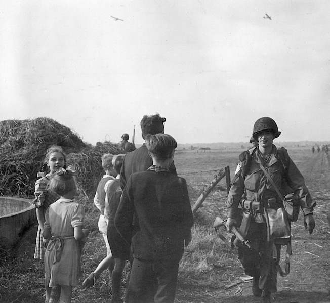 Although Operation Market-Garden ended in a bloody repulse, the initial air drop was executed with precision in daylight on September 18, 1944. Here, 101st Air- borne troops already on the ground move past Dutch civilians to a rallying point. Gliders approaching touchdown can be seen in the background.