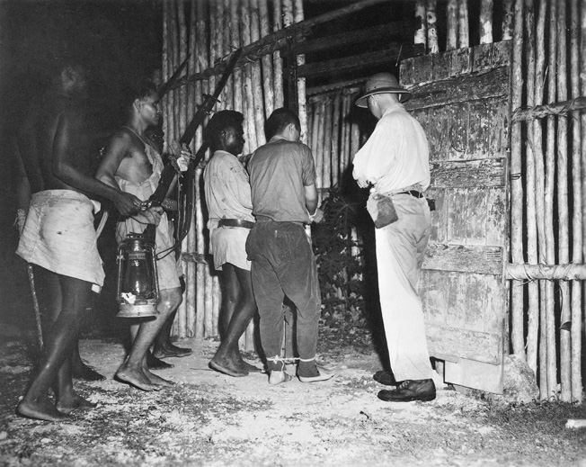An armed guard of native scouts trained and commanded by Captain D.G. Kennedy escorts a captured Japanese pilot into captivity at the Segi coast watchers' station on New Georgia in March 1943.