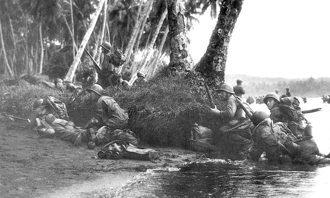 Attacking at the break of day in a heavy rainstorm, the first Marines ashore take cover behind tree trunks and and anything else they can find.