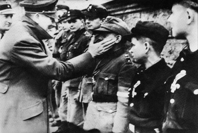 Baum’s unit fought against fanatical Germans as young as 14 and 15 during combat in the Ruhr Pocket. One of the last photos taken of the German dictator, the Führer rewards members of the Hitler Youth for their courageous stand in the defense of Berlin, March 1945.