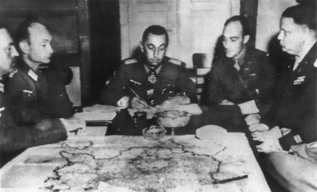 1st Lt. John Brunswick (formerly Hans Braunschweig of Bochum, Germany), XV Corps, Third U.S. Army, translates as General Friedrich Foertsch, chief of staff for General Albert Kesselring, commander of all German armies in Italy, Austria, and southern Germany, signs surrender documents. 