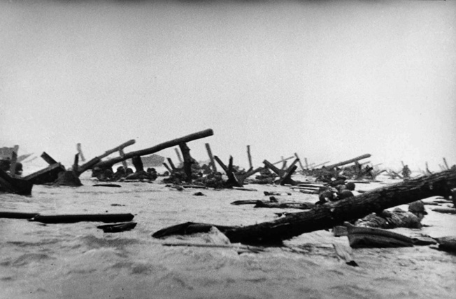 This photo taken by photographer Robert Capa, one of the few frames he captured on D-Day that survive, depicts American infantrymen struggling through the surf on Omaha Beach amid hedgehog and ramp obstacles placed by the Germans to disable landing craft.